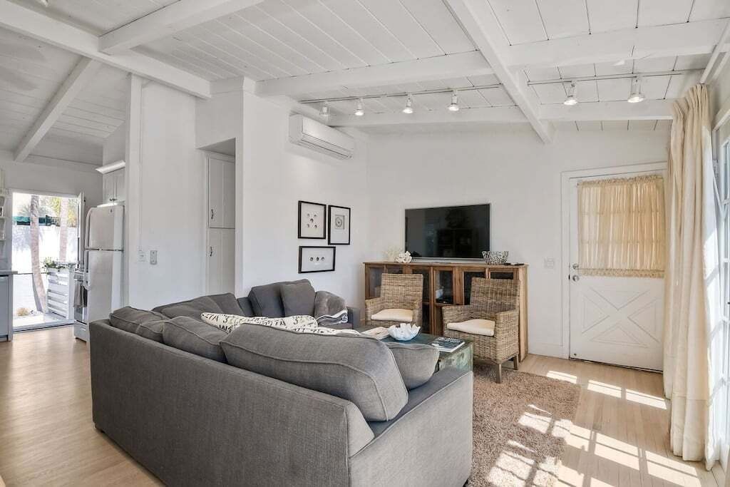 A modern living room with a grey sofa, wicker furniture, a television, and a door with curtains.