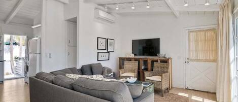 A modern living room with a grey sofa, wicker furniture, a television, and a door with curtains.