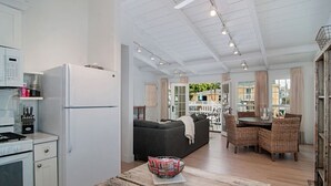 A modern kitchen with white appliances, a dining area with wicker furniture, and a cozy seating area with a dark sofa.