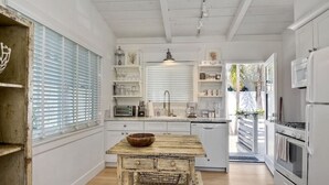 A kitchen with white cabinetry, a wooden table with a bowl, and a hanging light fixture.