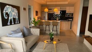 Ein modernes Wohnzimmer mit einer Couch, Sesseln, einem Couchtisch und einer Küche im Hintergrund.