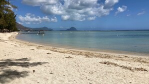 Ein Strand mit klarem türkisblauem Wasser, einer Holzpier und Bergen im Hintergrund.