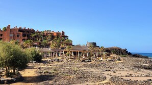 Un resort en la playa con varias edificaciones, palmeras y zonas de estar al aire libre.