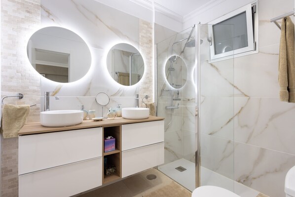 Une salle de bain moderne avec deux lavabos, une douche en verre et un meuble-lavabo avec un miroir.