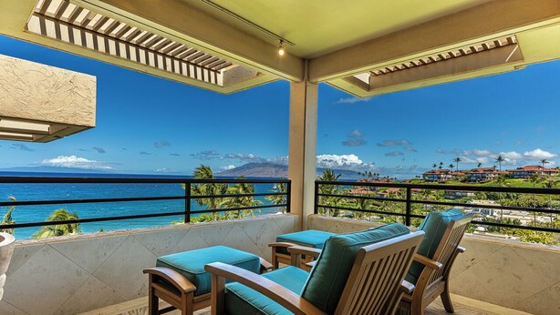 Een balkon met houten meubilair, uitzicht op de oceaan en een berg in de verte.