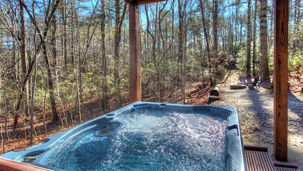 Un jacuzzi en zona boscosa con terraza de madera y un banco.