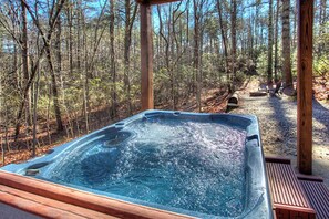A hot tub in a forested area with a wooden deck and a bench. - Southern Comfort - Spacious Family Retreat, Dog Friendly w/ Gaming Area and More (Sautee Nacoochee)