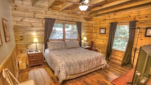 Un dormitorio de cabaña de madera con una cama, mesitas de noche, una silla y un escritorio.