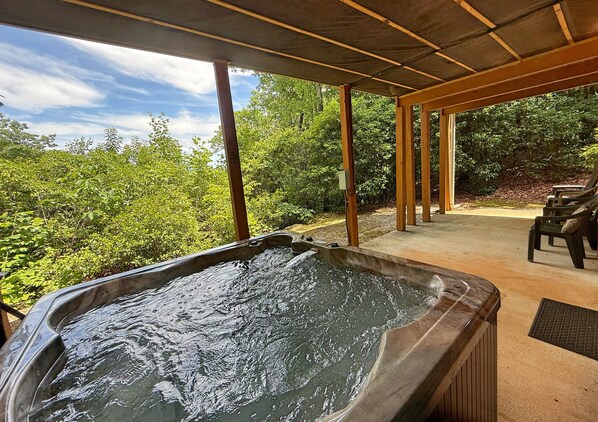Un bain à remous installé sous une pergola en bois, offrant une vue sur la verdure.