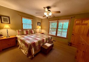 A bedroom with a bed, two bedside tables, a ceiling fan, and two windows with blinds.