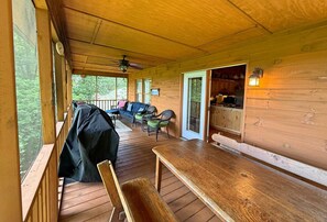 Eine überdachte Veranda mit einer hölzernen Bank, einem Esstisch und einem Grill.