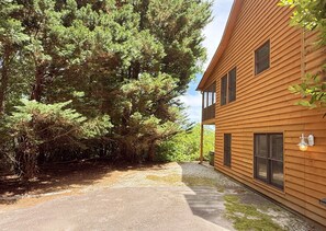 Une cabane en bois avec une allée en gravier, entourée d’une forêt dense.
