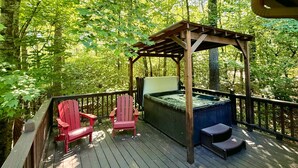 Una terraza de madera con dos sillas Adirondack rojas, un jacuzzi y una pérgola.