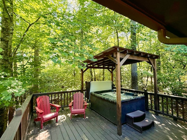 Una terraza de madera con dos sillas Adirondack rojas, un jacuzzi y una pérgola.