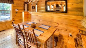 A wooden cabin interior with a dining table, chairs, a chandelier, and a mirror.