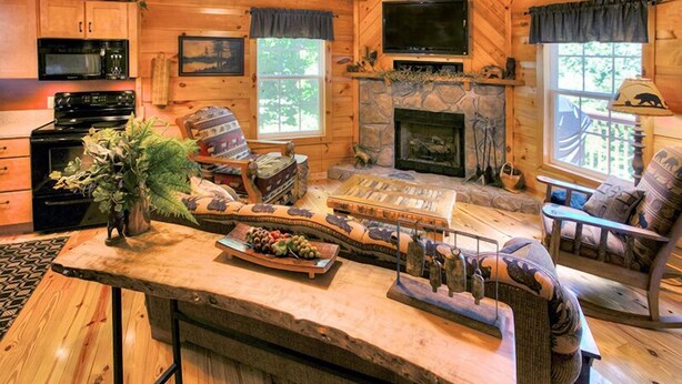 A cozy cabin interior with a stone fireplace, wooden furniture, and a dining area.