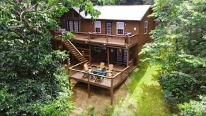 A two-story wooden cabin with a deck and outdoor seating area, surrounded by dense greenery.