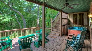 A wooden deck with green Adirondack chairs, a hot tub, and a staircase leading to an upper level.