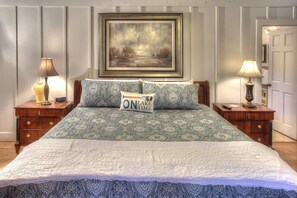 A bed with patterned bedding, a pillow with "ON LAKE TIME" text, and a framed painting above.