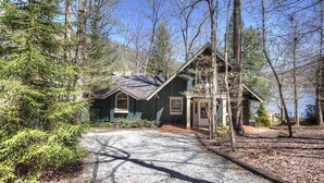 A cabin with a gravel driveway, surrounded by trees and a body of water.