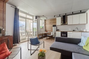 Un apartamento moderno con cocina, comedor y sala de estar. Cuenta con un ventanal grande, un sofá, una mesa de comedor y una cocina con armarios y electrodomésticos blancos.