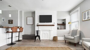 Una sala de estar moderna con chimenea, un televisor de pantalla plana montado encima, un sofá, un sillón y una mesa de centro.