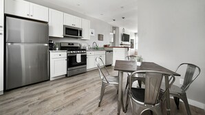 Una cocina moderna con electrodomésticos de acero inoxidable, armarios blancos, una mesa de comedor de madera y sillas de metal.
