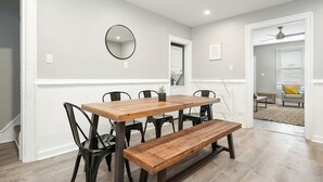 Un comedor con una mesa de madera, sillas negras y un banco. Hay un espejo en la pared y una puerta que da a otra habitación.