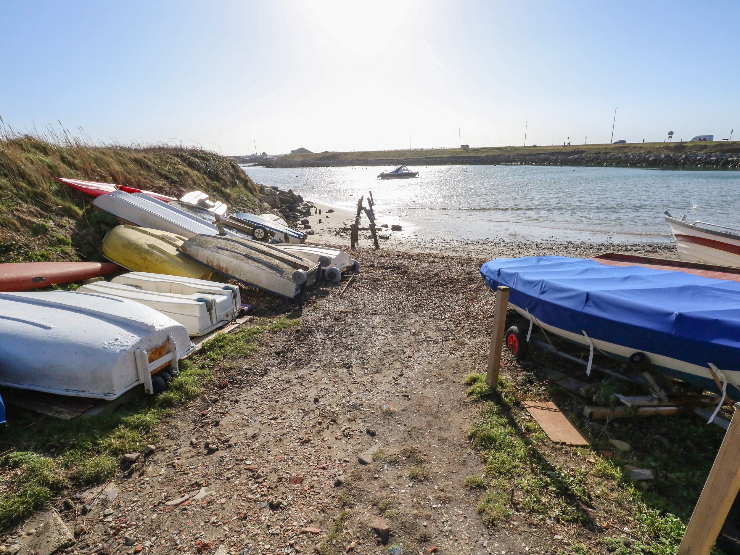 A gravel path leading to a body of water with boats lined up on the shore.