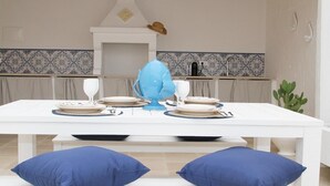 Mesa de jantar posta com pratos, copos e talheres, com dois almofadas azuis de cada lado.