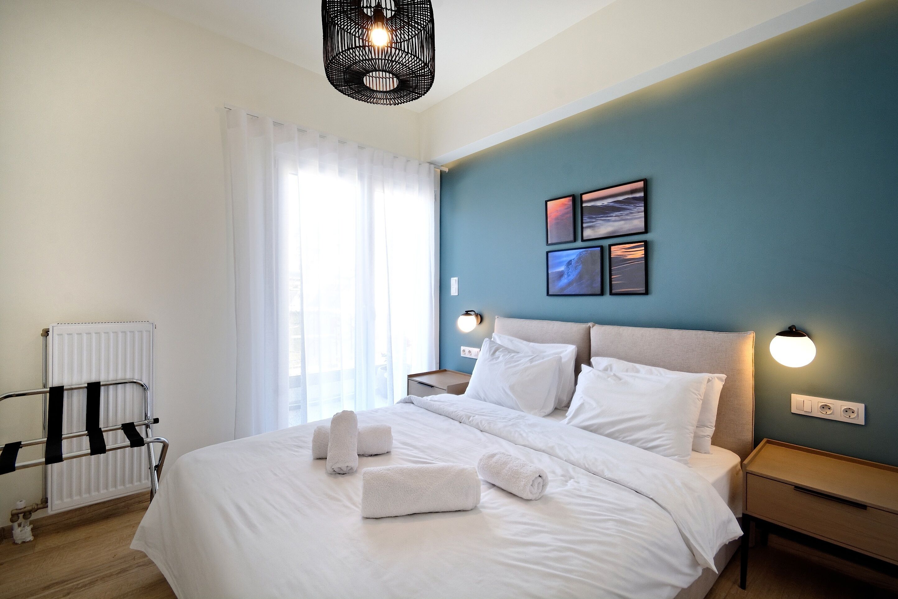 A neatly made bed with white linens and towels, a bedside table with a lamp, and a wall with framed pictures.