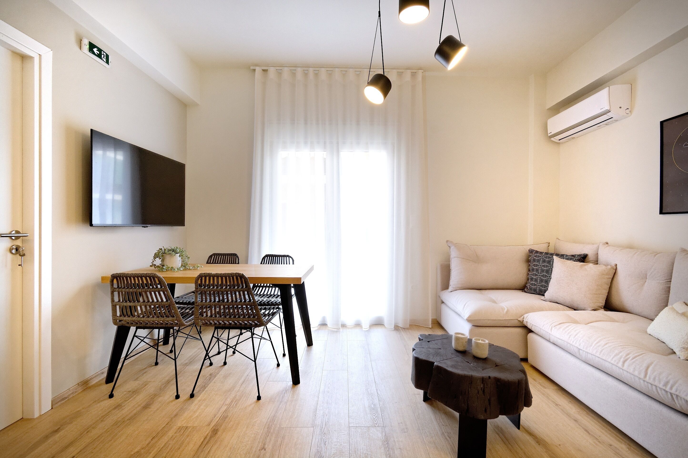 A modern living room with a sofa, a dining table with chairs, a flat-screen TV, and an air conditioning unit.