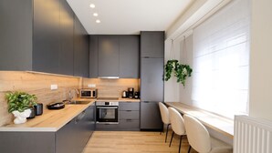 Una cocina moderna con armarios oscuros, encimera de madera, horno empotrado, microondas y una zona de comedor con vistas al exterior.