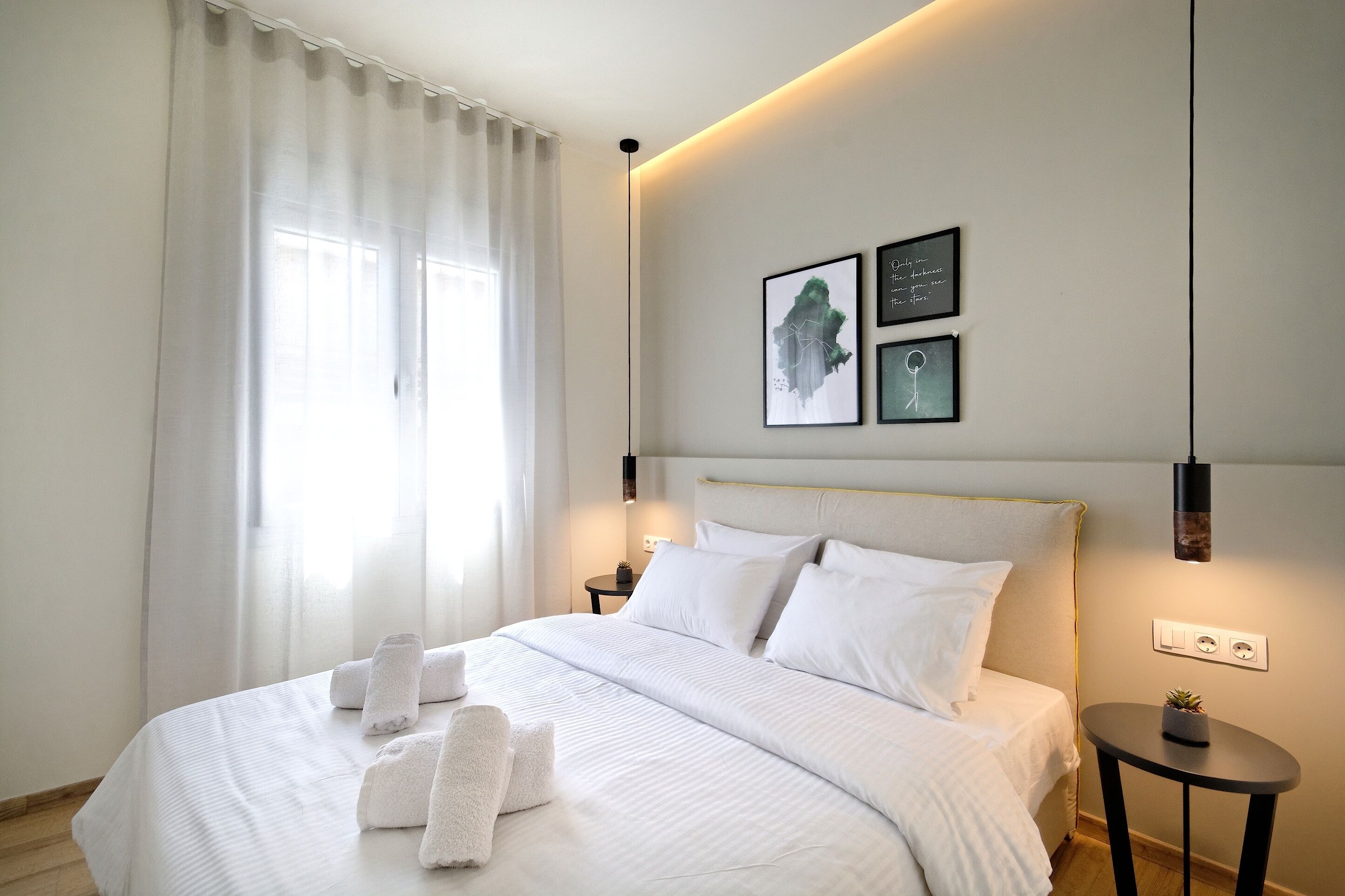 Una cama bien hecha con sábanas y toallas blancas, una mesita de noche con una planta y una obra de arte en la pared.