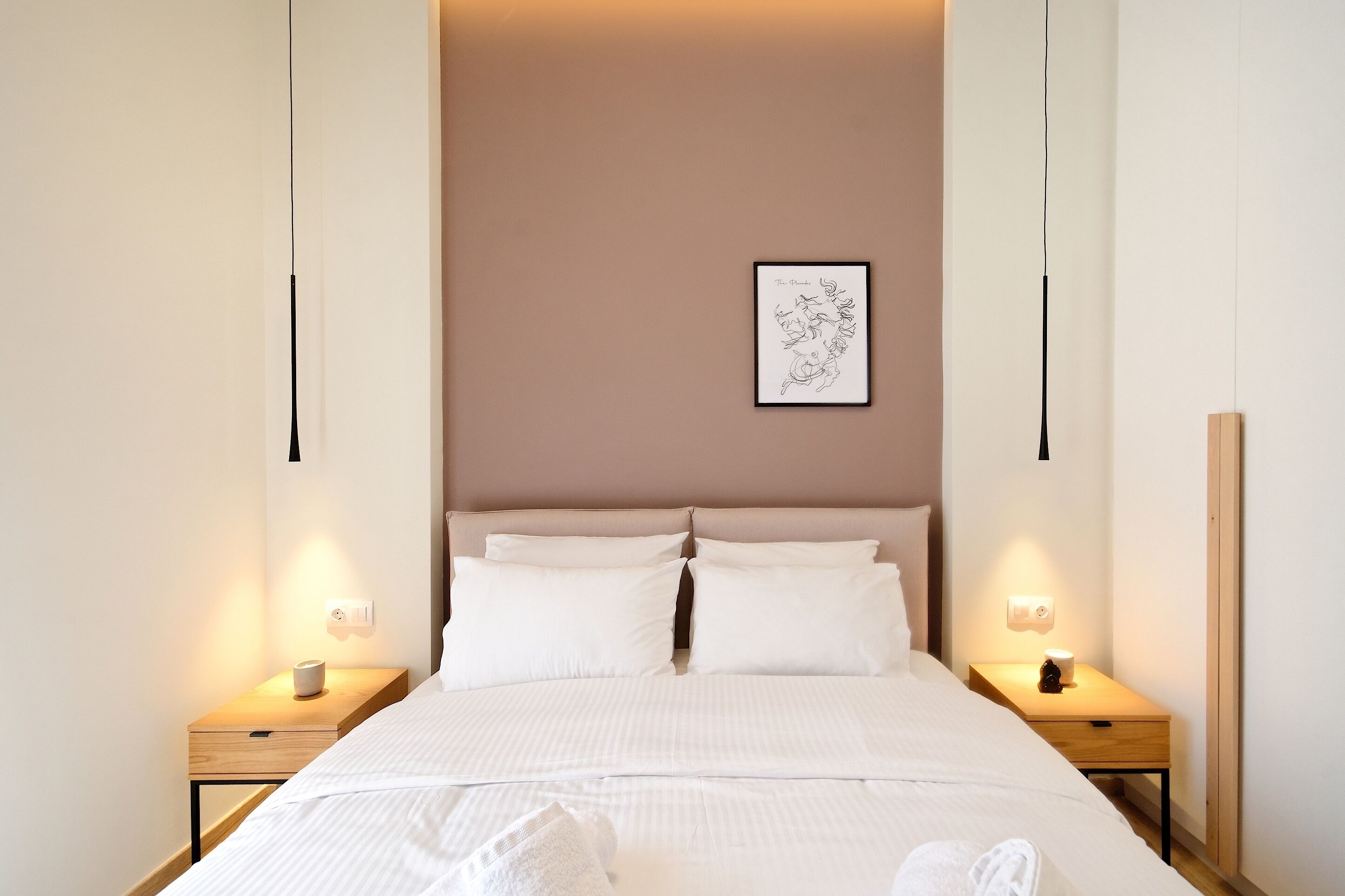 Un lit bien fait, avec du linge de lit blanc, deux tables de chevet avec des lampes et une œuvre d’art encadrée au mur.