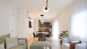 Una sala moderna con sofá, reposapiés y una mesita de centro. Se aprecia un comedor con una mesa y sillas al fondo.
