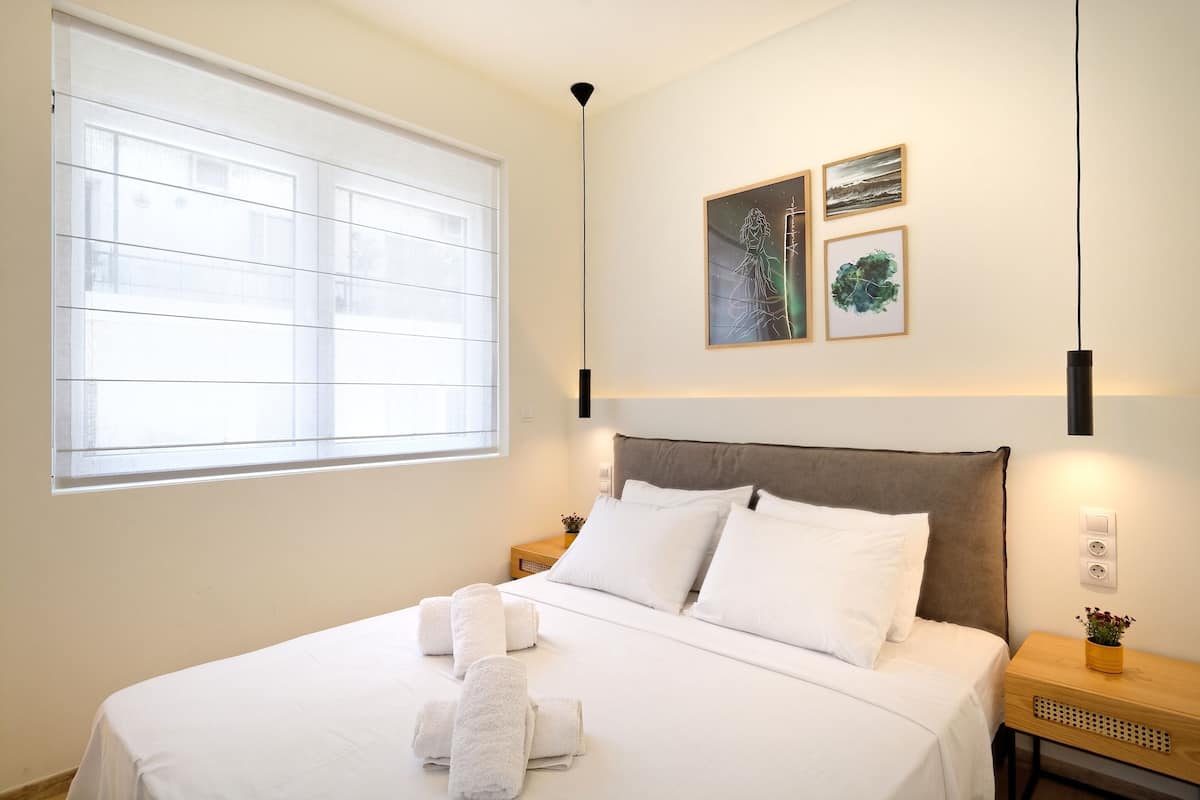 Ein ordentlich bezogenes Bett mit weißen Leinen und Handtüchern, ein Nachttisch mit einer Pflanze und ein Bild an der Wand.