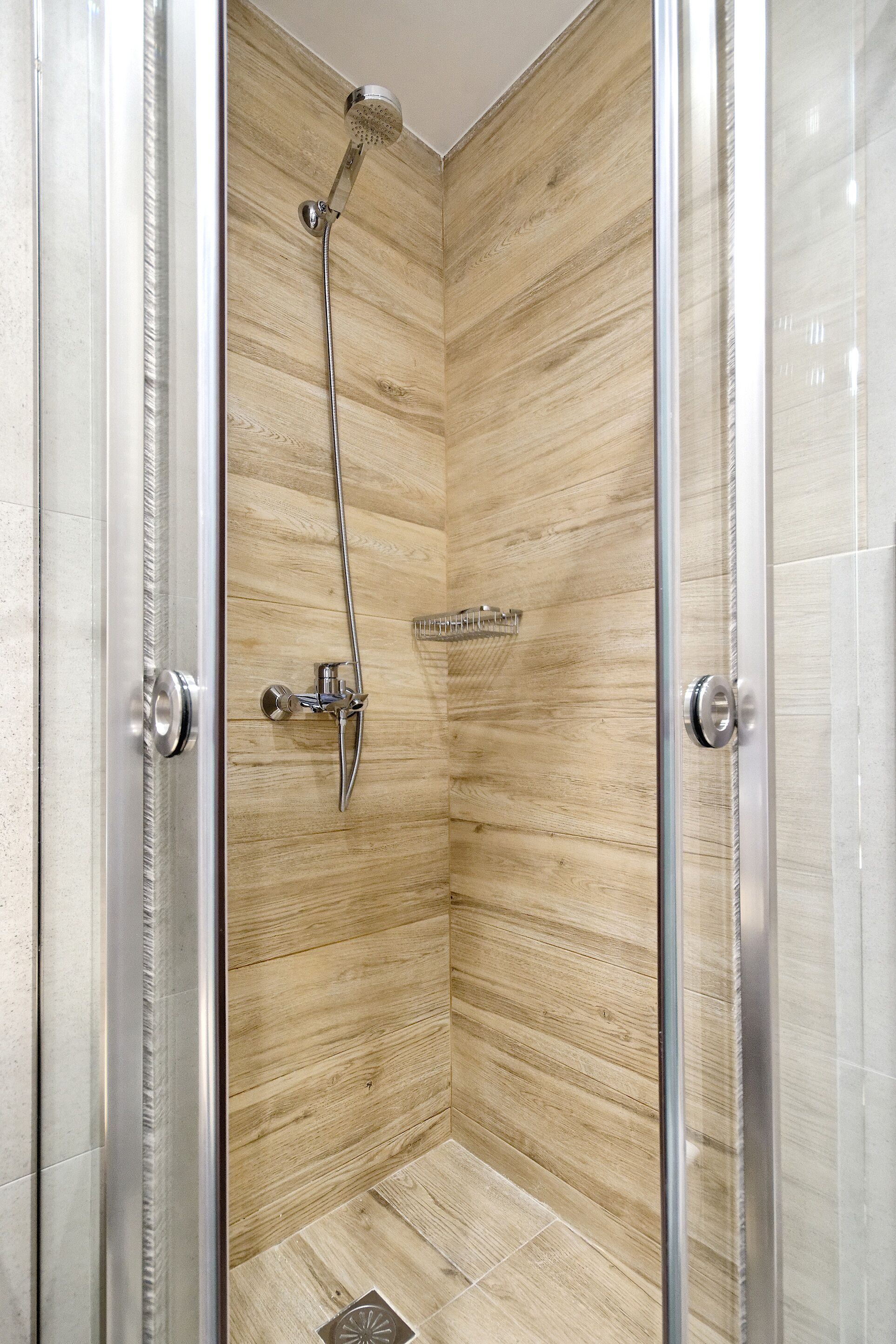 A walk-in shower with a wooden panel wall, a glass door, and a showerhead.