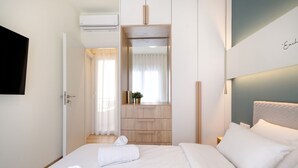 Habitación de hotel con cama, mesita de noche, televisor montado en la pared y ventana con cortinas.