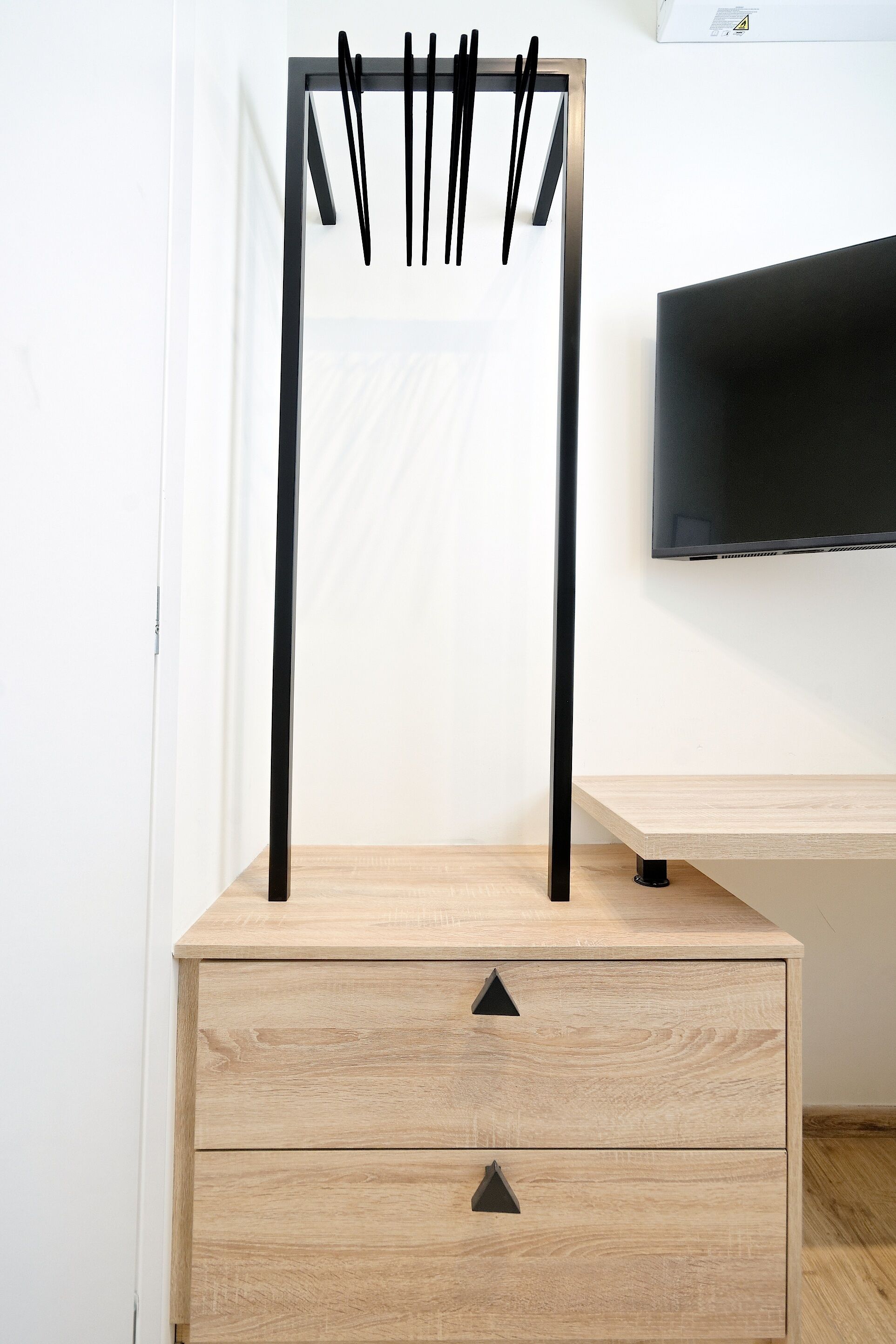 A minimalist wooden dresser with two drawers and a TV mounted on the wall above.