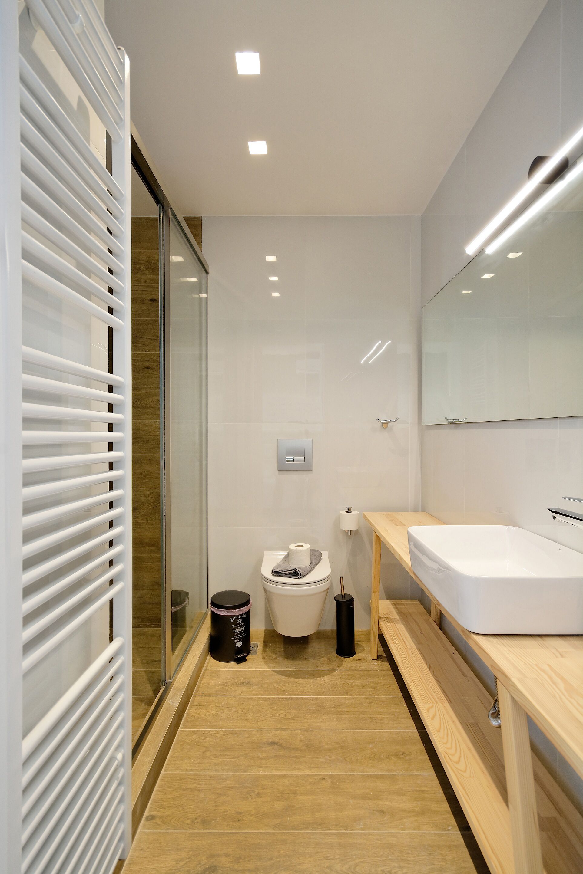 A modern bathroom with a glass shower enclosure, a wooden vanity, and a large mirror.