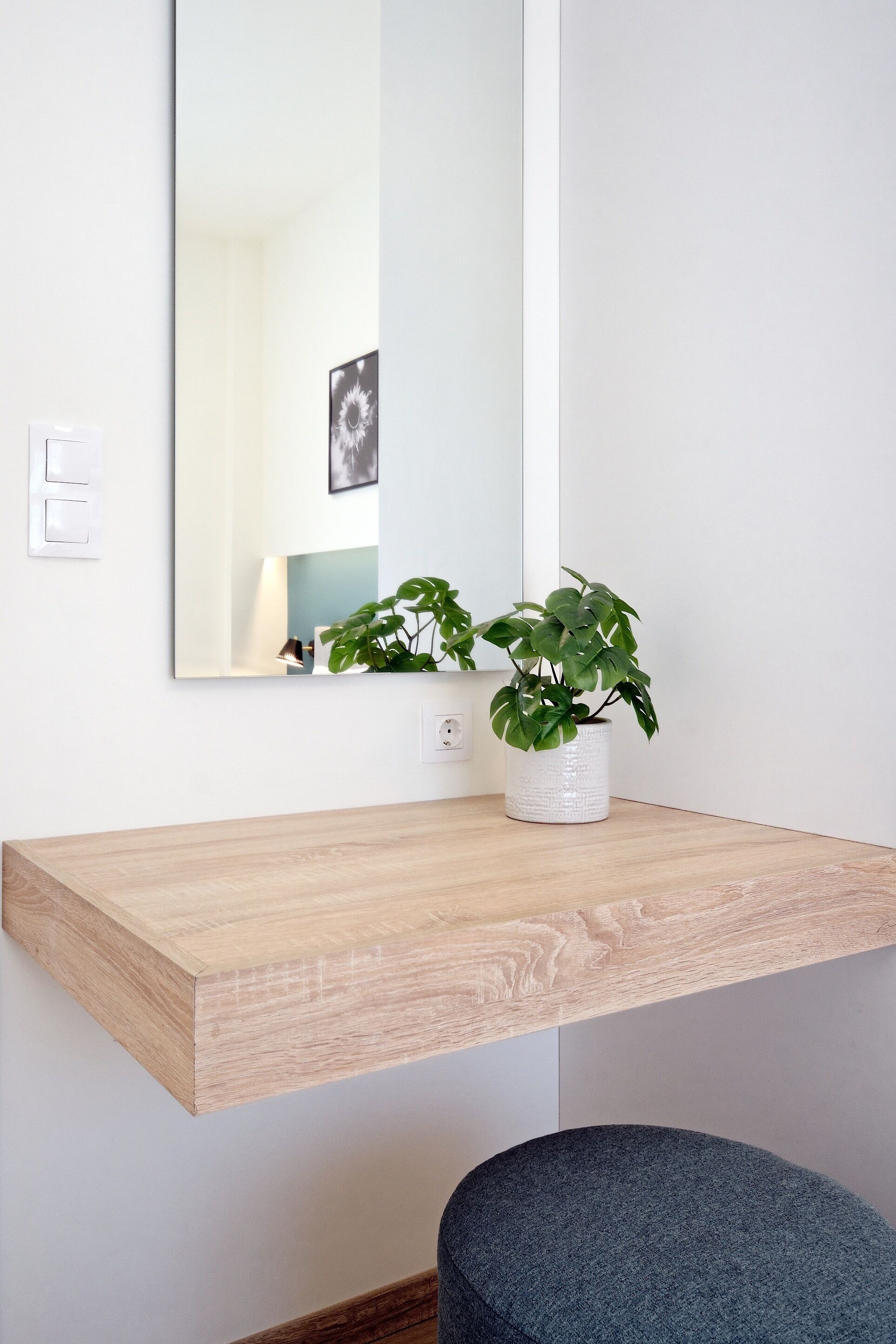 Un baño minimalista con tocador de madera, lavabo blanco, planta en maceta y espejo.