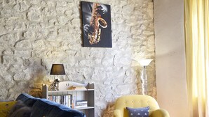 Un salon avec un mur en pierre, un fauteuil jaune, une bibliothèque et une lampe.