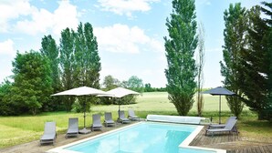 Une piscine rectangulaire dotée d’une terrasse en bois, entourée de chaises longues et de parasols.
