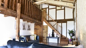 Un intérieur rustique avec des poutres apparentes, un escalier, un canapé et une petite table agrémentée d’objets décoratifs.