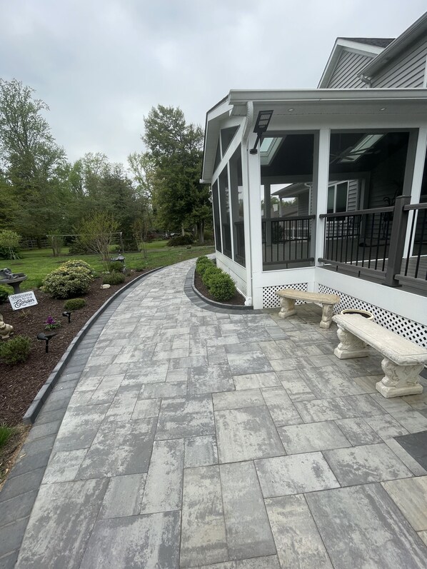 A covered patio area with stone flooring, a bench, and a 'Welcome Garden' sign.