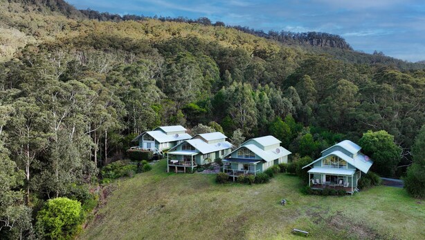 A cluster of modern, light-colored houses with flat roofs, surrounded by dense forest and hills. - Valley Vista - Three bedroom villa located on golf course with amazing views! (Kangaroo Valley)
