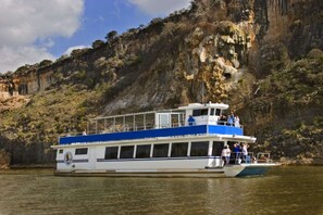 A riverboat with a blue upper deck and white lower deck, passengers on the upper deck, and a rocky cliff in the background. - Perfect Private Getaway in Buchanan Lake Village! (Tow)