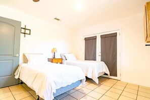 A hotel room with two beds, a nightstand, a lamp, a door, and a cross on the wall. - Perfect Private Getaway in Buchanan Lake Village! (Tow)