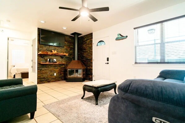 A living room with a fireplace, a ceiling fan, and a large window. - Perfect Private Getaway in Buchanan Lake Village! (Tow)